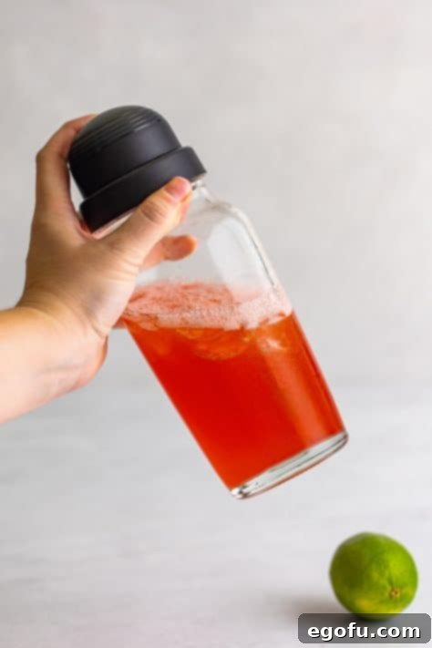 Hand shaking the cocktail shaker with ingredients inside.