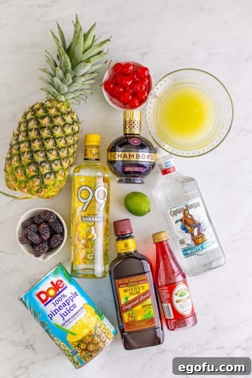 All the essential ingredients for a Rum Runner Cocktail laid out: ice, light rum, dark rum, banana liqueur, Chambord, pineapple juice, lime juice, grenadine, and garnishes like fresh blackberries, lime, pineapple, and maraschino cherries.