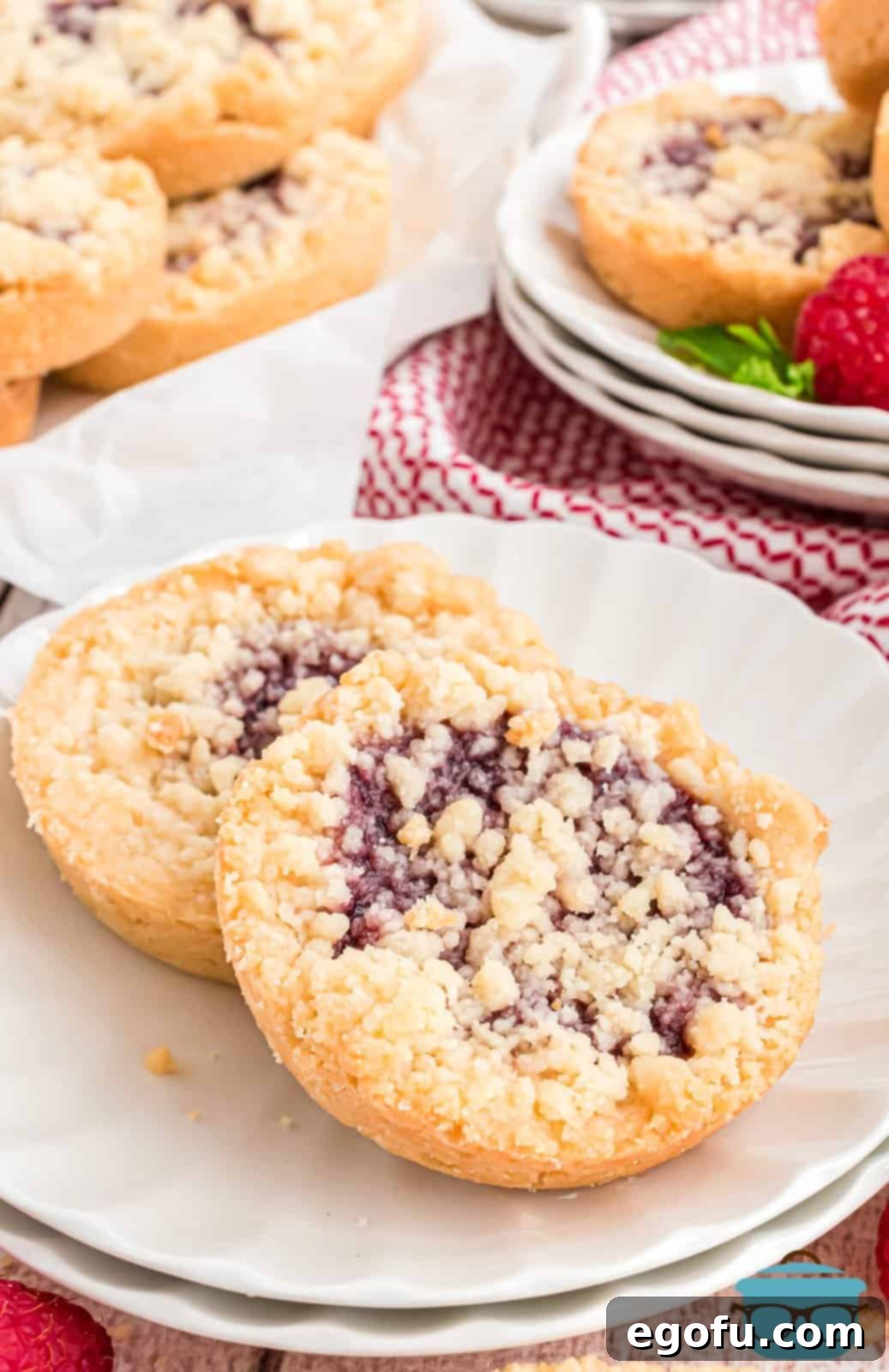 Two perfectly baked Raspberry Tartlets resting elegantly on a pristine white plate, showcasing their golden crust and glistening raspberry filling.