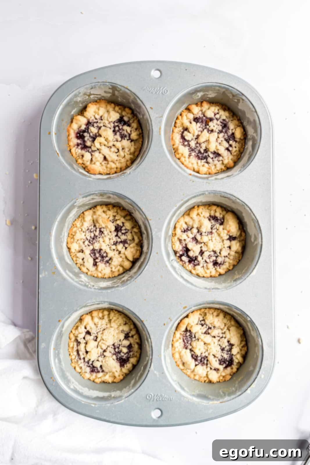 A tantalizing view of the freshly baked raspberry tartlets, golden and bubbling, still warm in their muffin tin after coming out of the oven.
