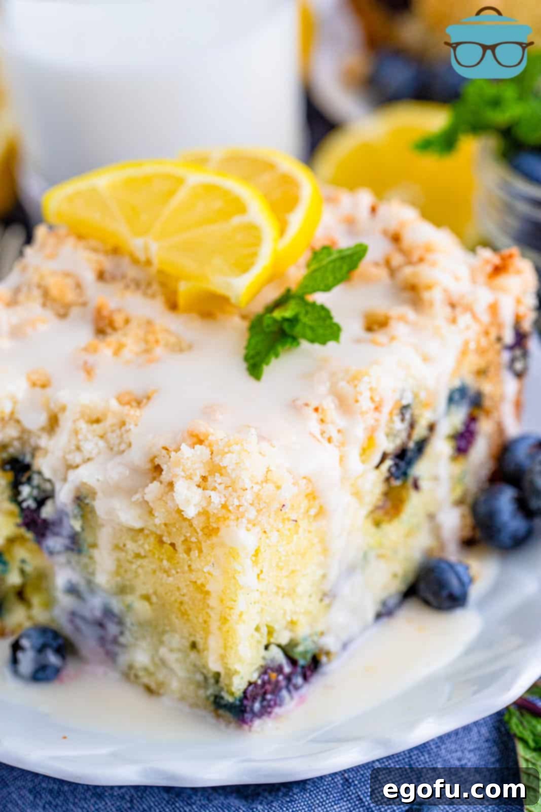 Slice of Lemon Blueberry Coffee Cake on plate topped with glaze, lemon slices and mint.