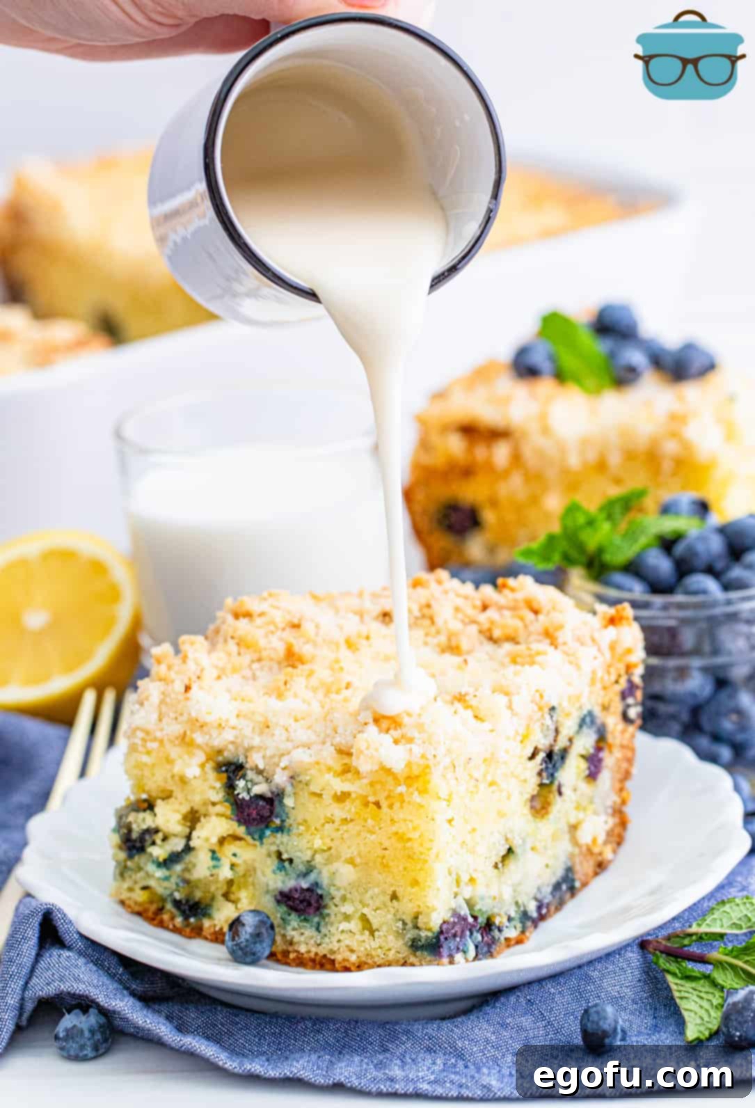 Glaze being poured over a slice of Lemon Blueberry Coffee Cake on white plate.