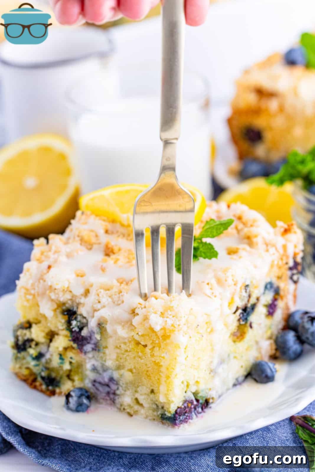Fork going into a slice of Lemon Blueberry Coffee Cake on white plate.