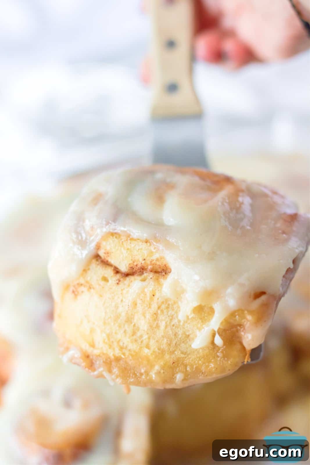 A metal spatula holding up one of the freshly baked Tik Tok Cinnamon Rolls, showcasing its gooey texture and generous icing.