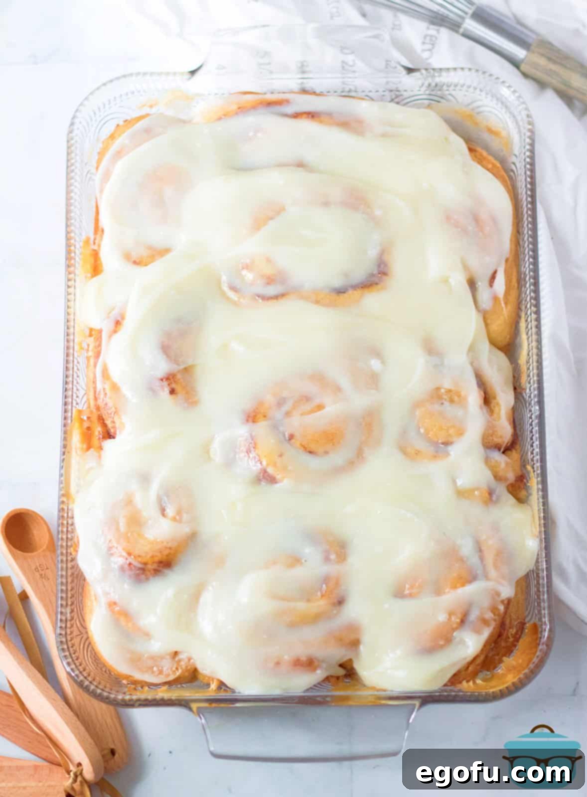 A beautifully composed shot of several heavy cream cinnamon rolls in a baking dish, glistening with icing and ready to be served.