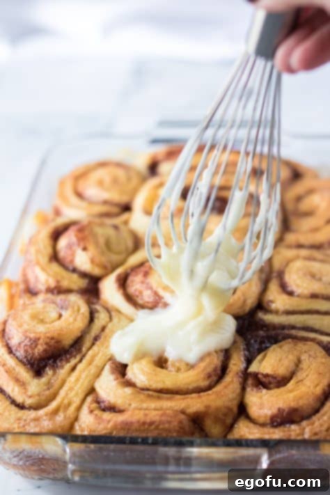 Icing being spread over baked cinnamon rolls.