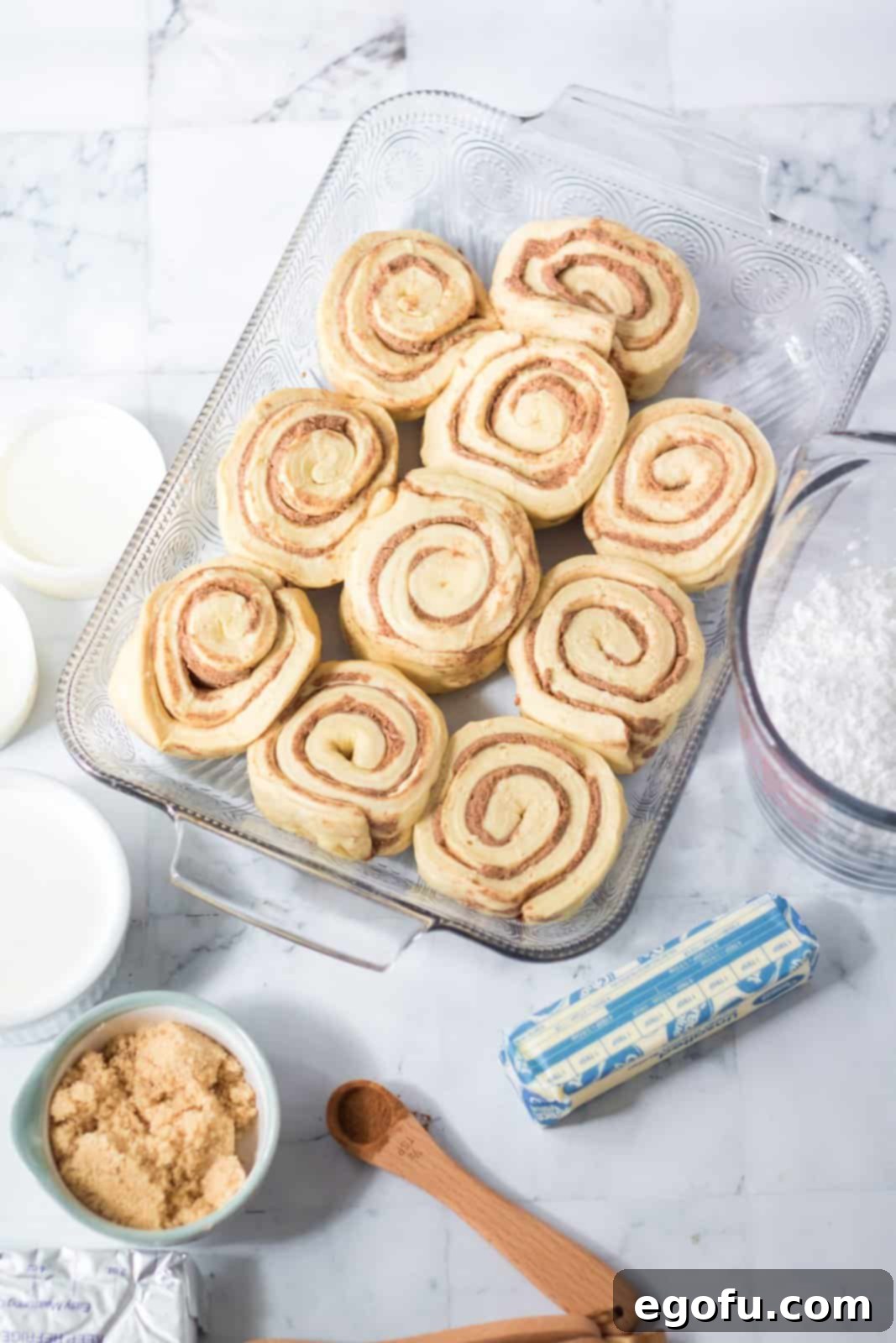 All the essential ingredients for Tik Tok Cinnamon Rolls laid out: refrigerated Grands cinnamon rolls, heavy whipping cream, butter, brown sugar, ground cinnamon, cream cheese, and powdered sugar.