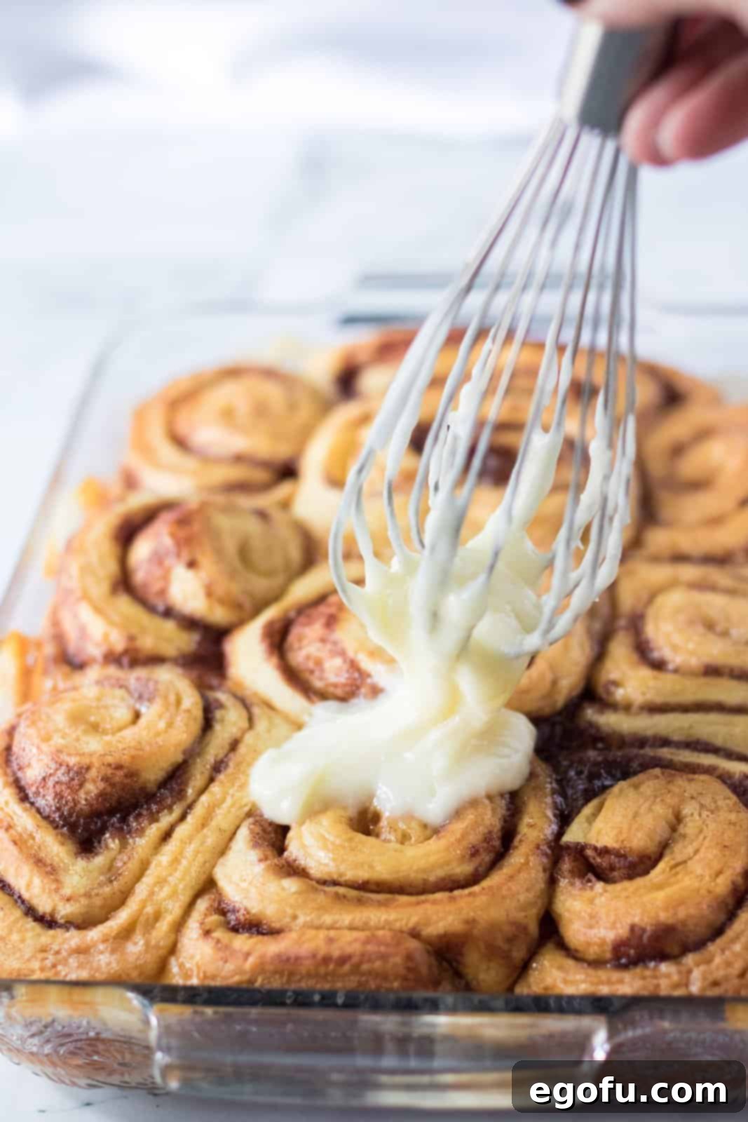 Homemade cream cheese icing being spread generously over the warm, baked Tik Tok Cinnamon Rolls in the pan.