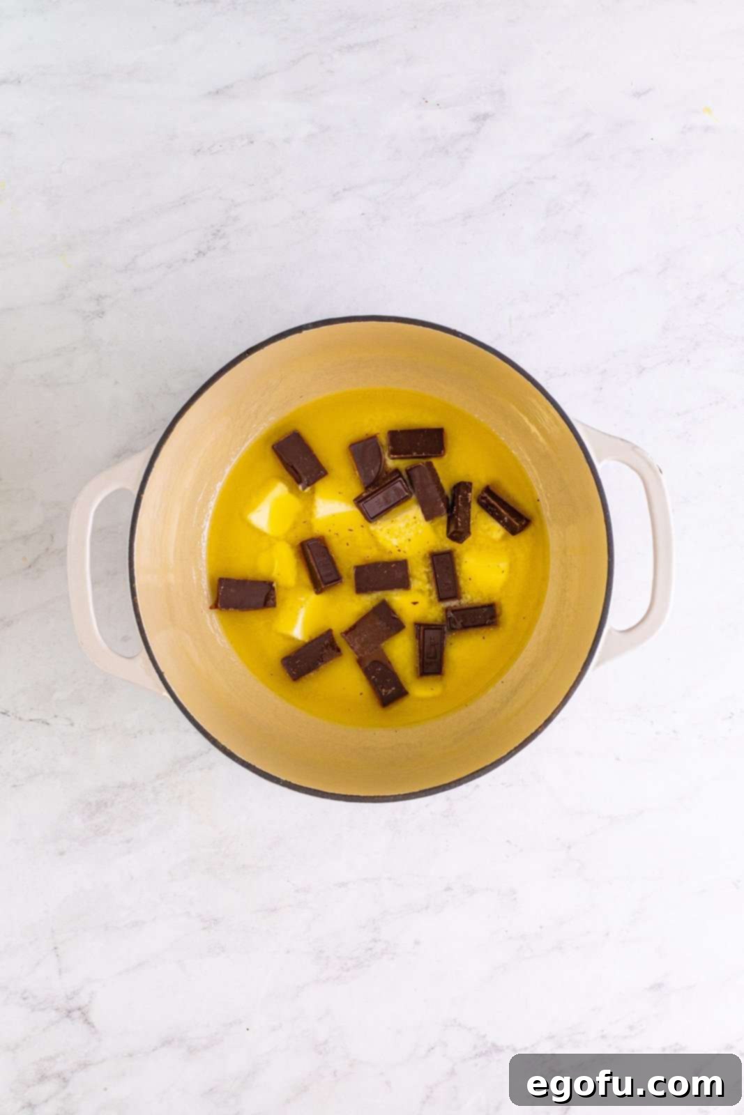 Melted butter with chunks of German chocolate baking bar in a Dutch oven, ready to be stirred.