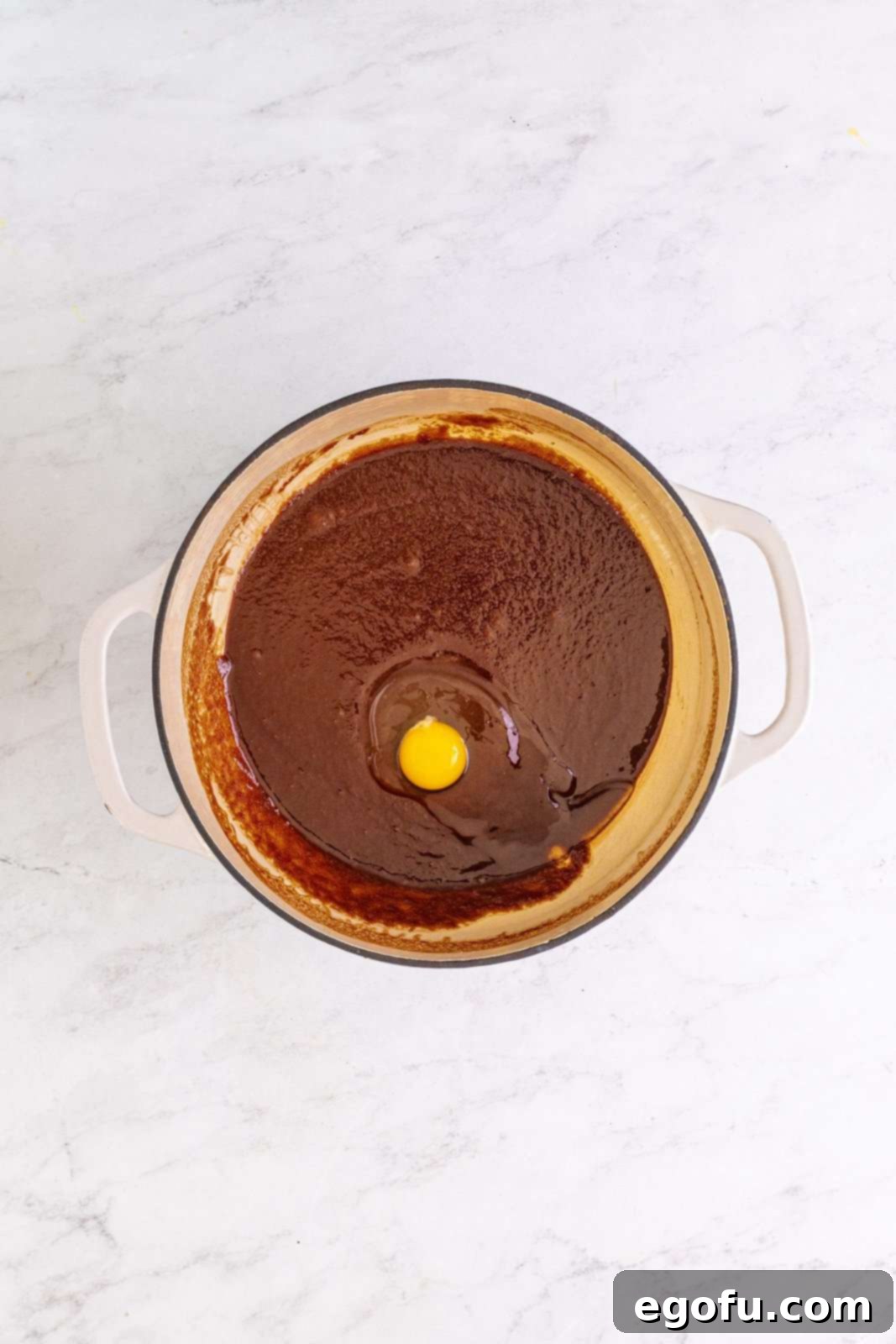 Eggs being whisked one by one into the chocolate and sugar mixture in the pot.
