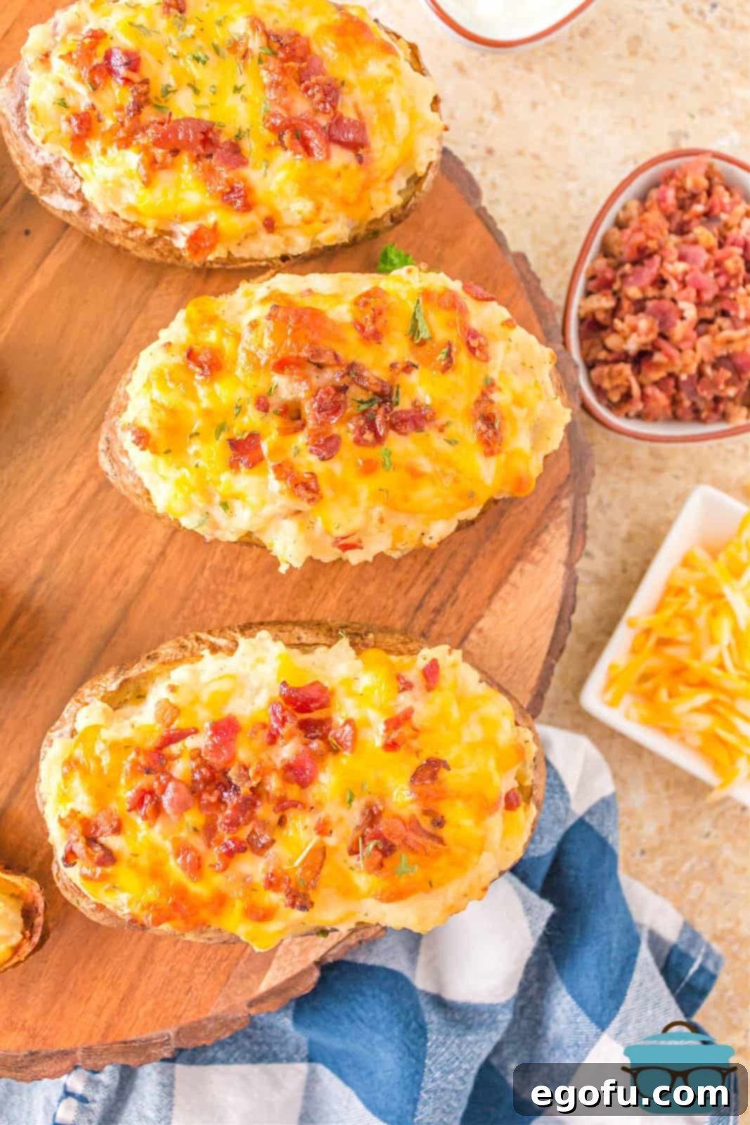 Overhead view of finished Grilled Twice Baked Potatoes arranged beautifully on a round wooden serving board, showcasing their golden-brown skin and rich toppings.