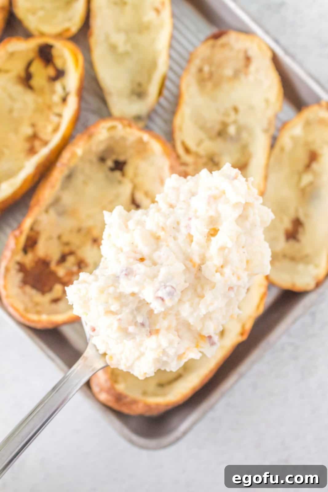 A spoon actively stuffing creamy potato mixture back into the hollowed-out potato skins, creating generous mounds of filling.
