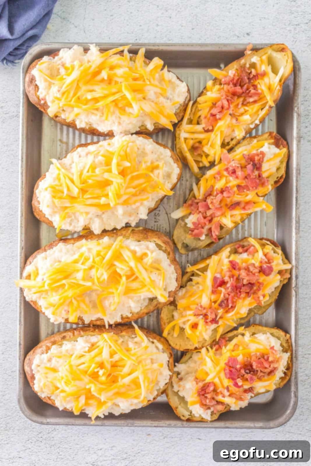 Stuffed potatoes generously topped with extra shredded cheese and bacon bits, ready for the final grilling step.