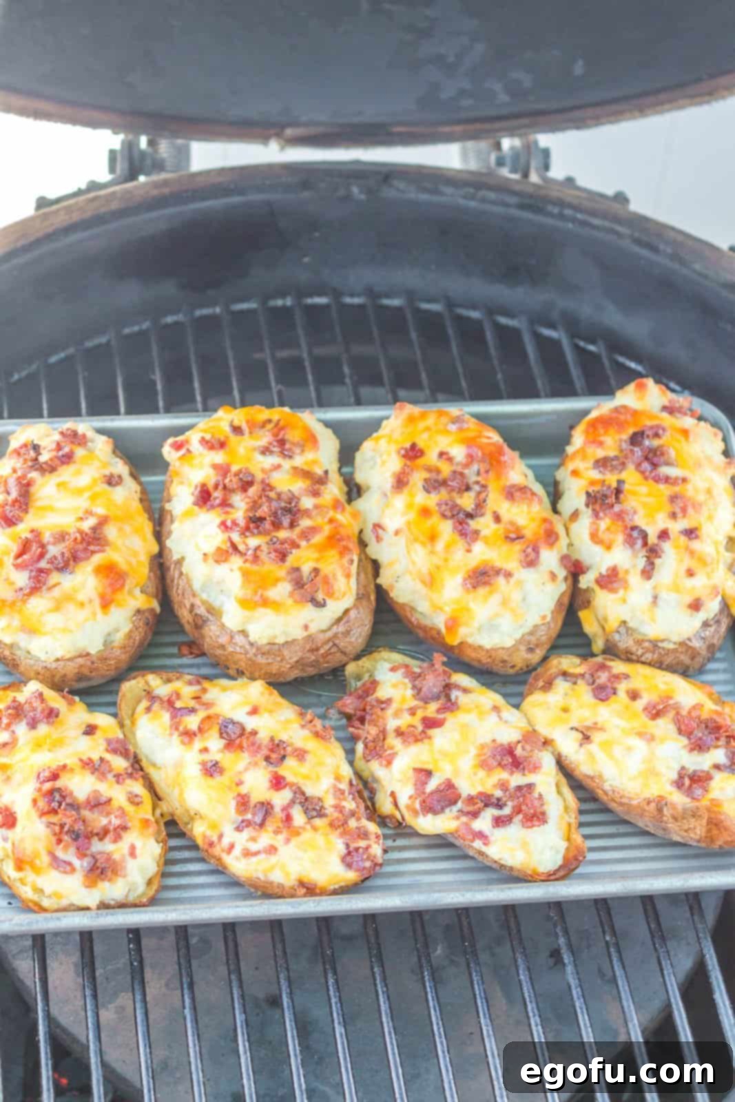 Tray of stuffed and topped potatoes placed back on the grill over indirect heat for the final stage of cooking, where cheese will melt.