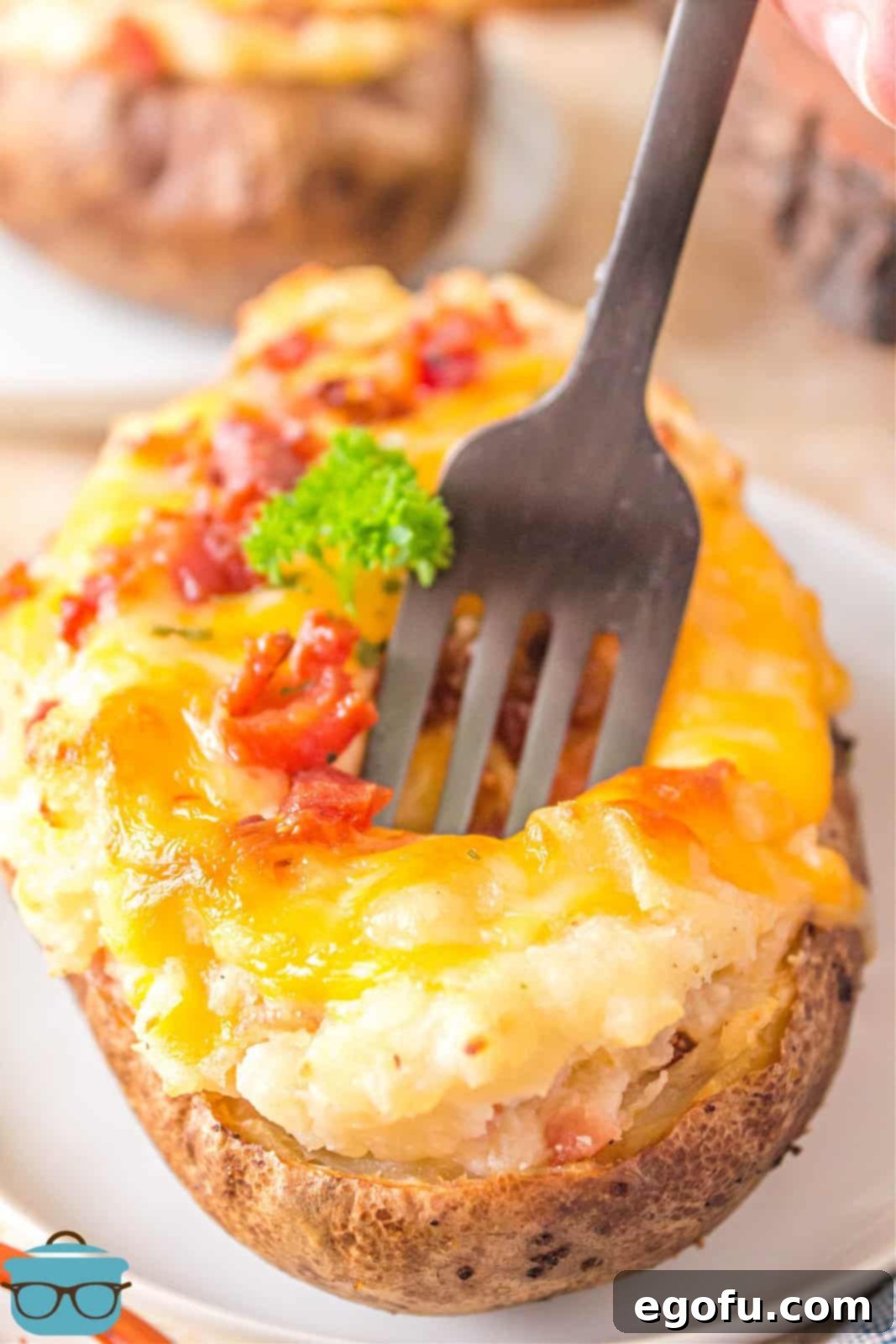 A fork piercing into one of the finished Grilled Twice Baked Potatoes, revealing the creamy interior and crispy toppings.