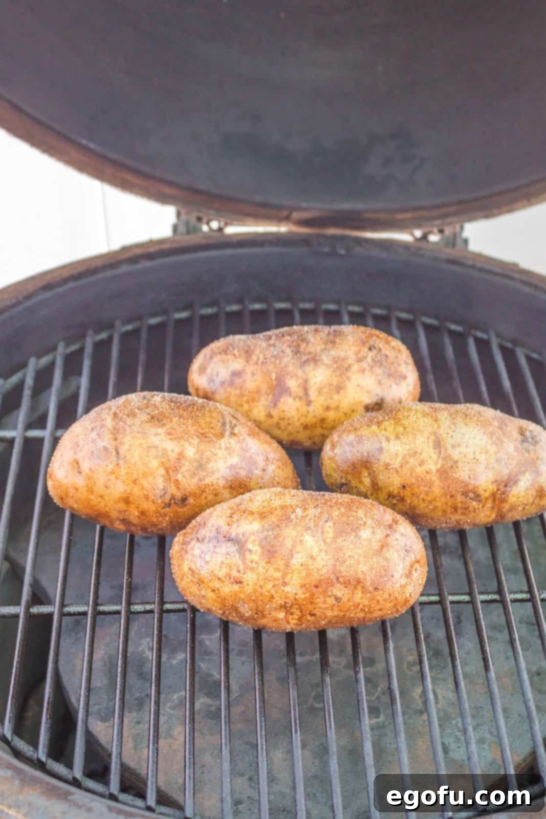 Poked and seasoned potatoes carefully placed on the grill grates over the indirect heat zone, ready for the first bake.