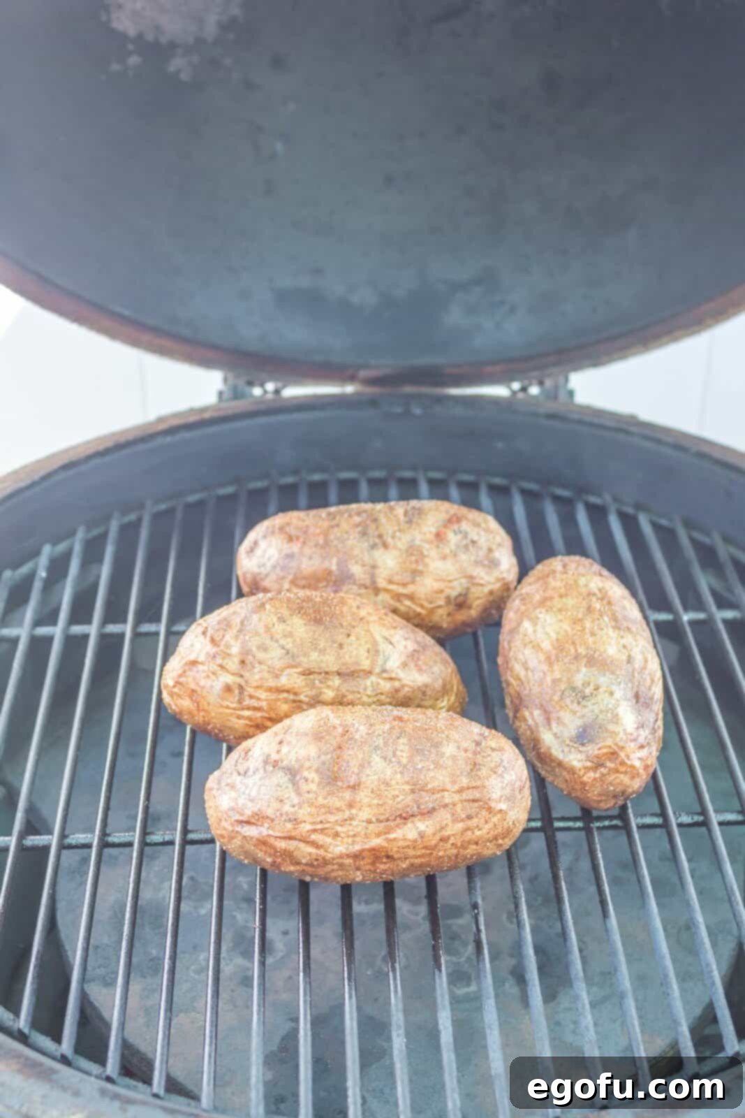 Fully cooked potatoes on the grill grates, showing crispy skins and a tender appearance after the first grilling stage.