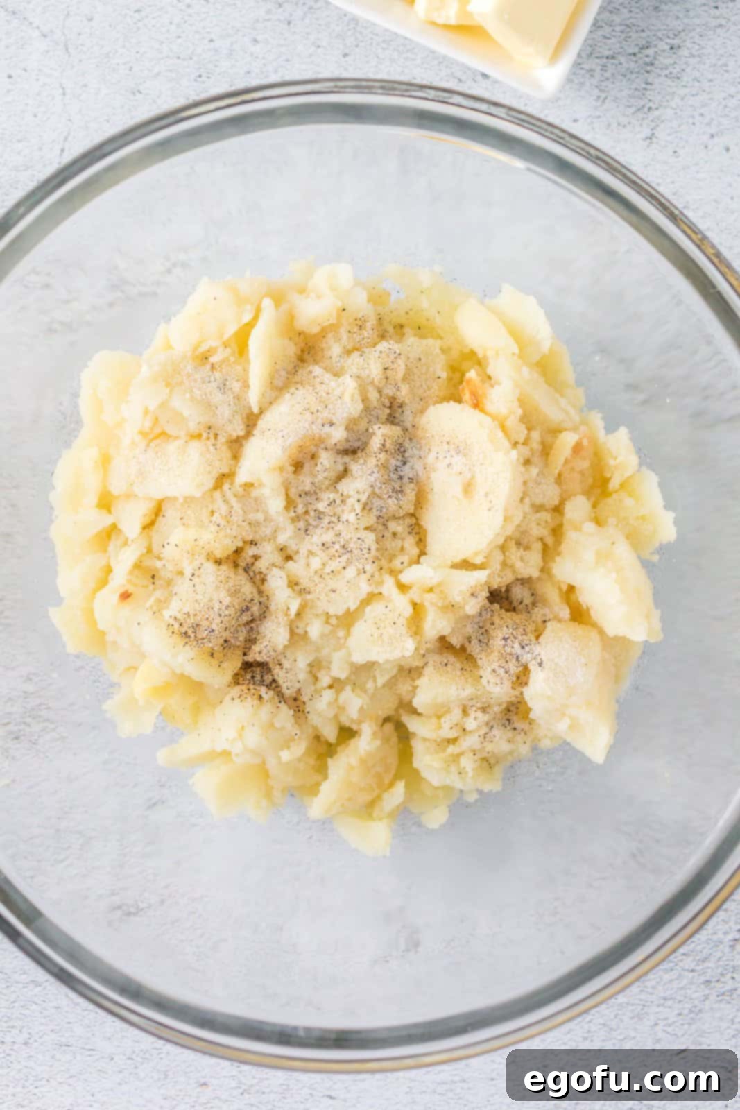 Scooped out potato flesh in a mixing bowl, combined with salt, onion powder, pepper, chicken broth, and melted butter, ready for blending.