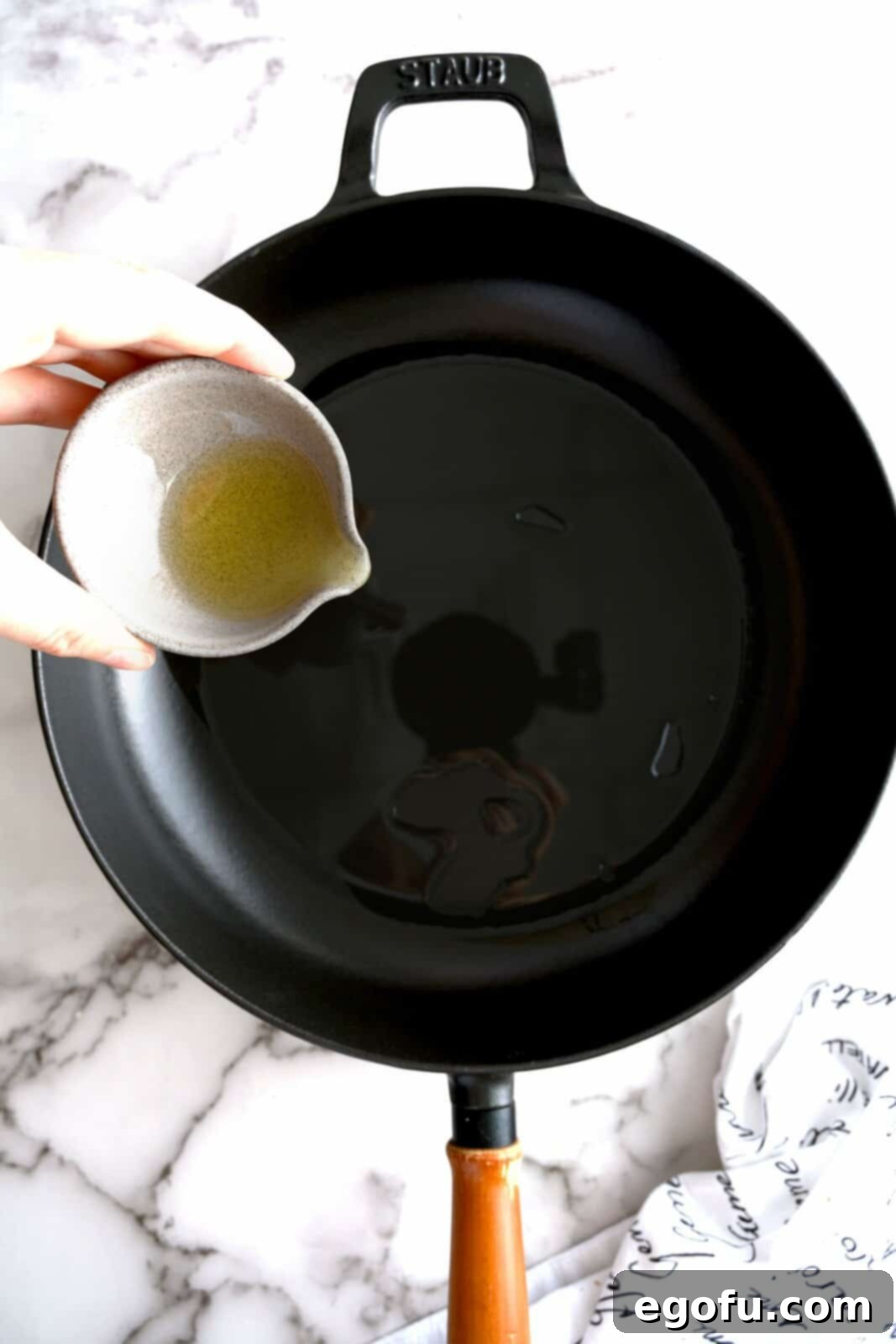 Olive oil being added to a hot cast iron skillet.
