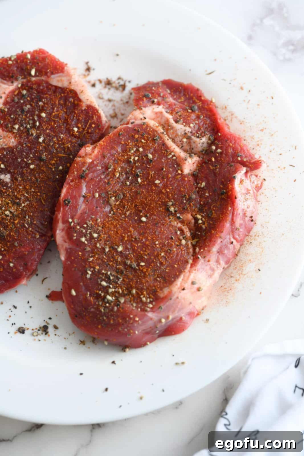 Steaks seasoned liberally on a white plate, ready for searing.
