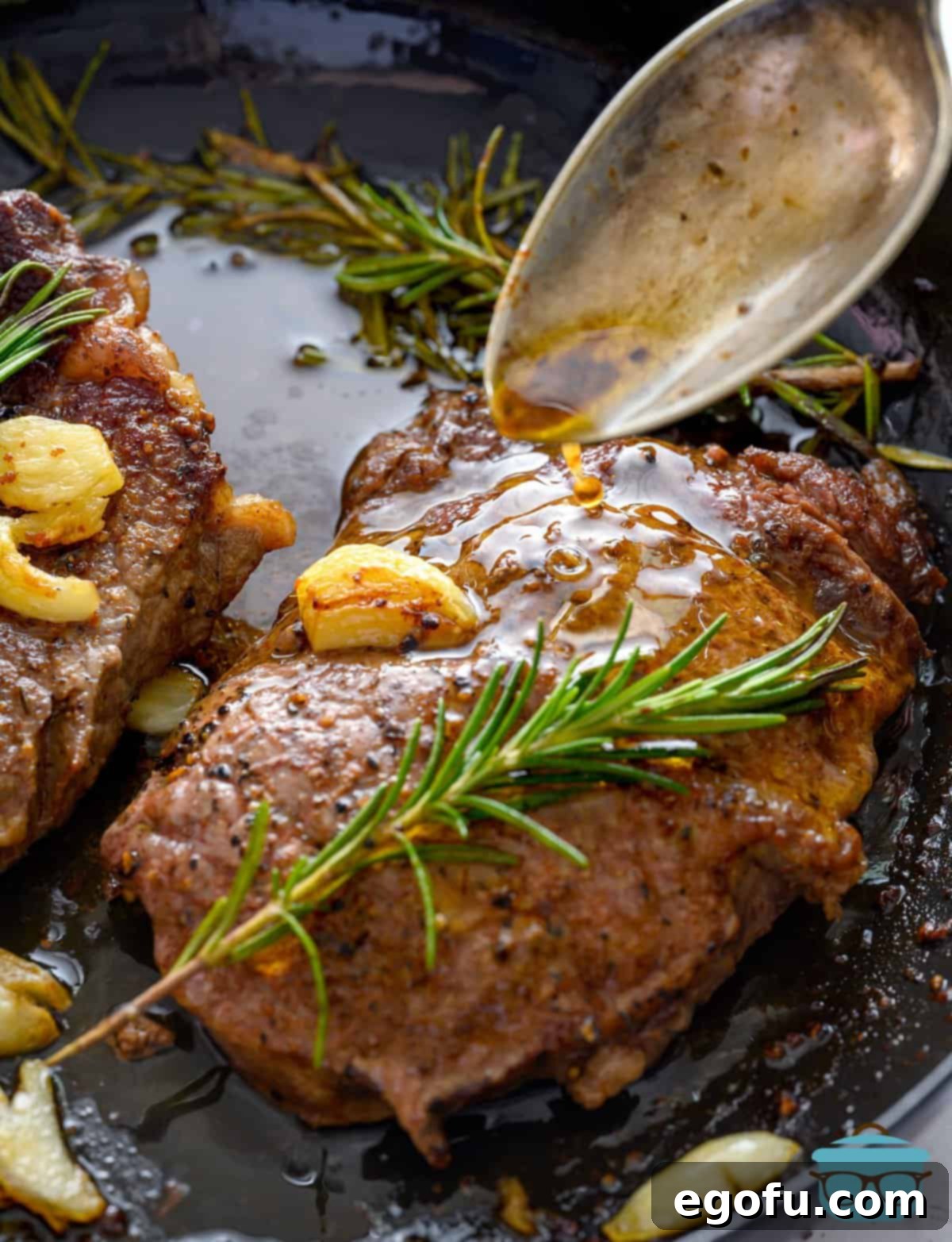 Close-up of a spoon dripping flavorful pan drippings over a sizzling Pan Seared Steak in a cast iron pan.