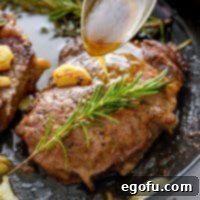 Close up square image of a Pan Seared Steak in skillet with a spoon dripping pan drippings over it, showing a delectable crust.