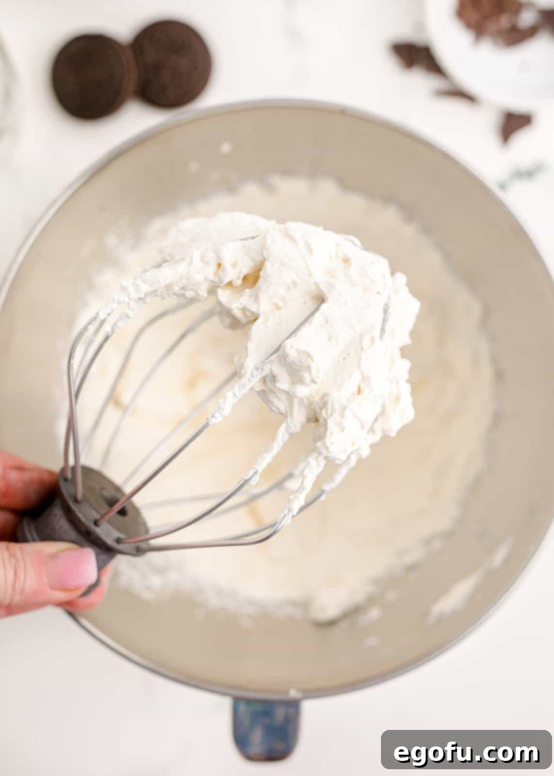 Finished homemade whipped cream on the beater attachment of a stand mixer, showing stiff peaks.