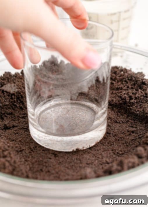 Oreo crust being pressed into pie plate with cup.