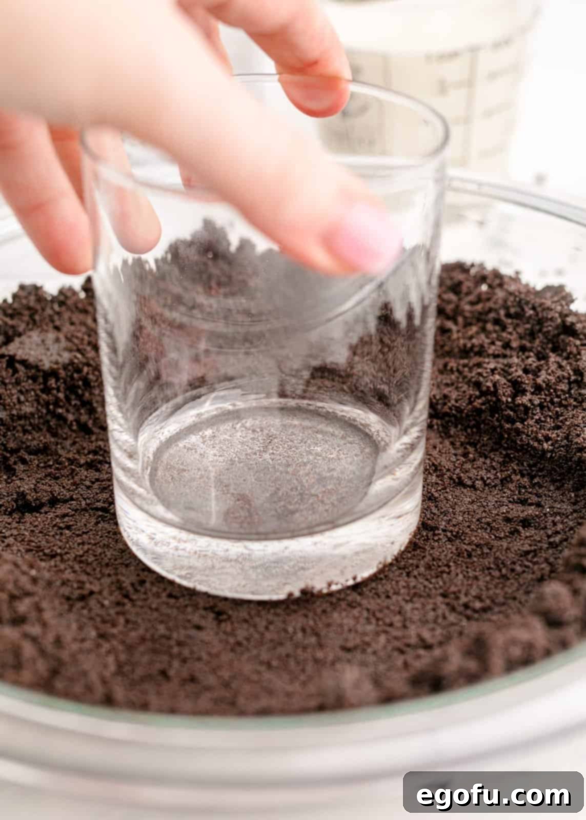Oreo crust being pressed into a pie plate with the bottom of a glass for an even layer.