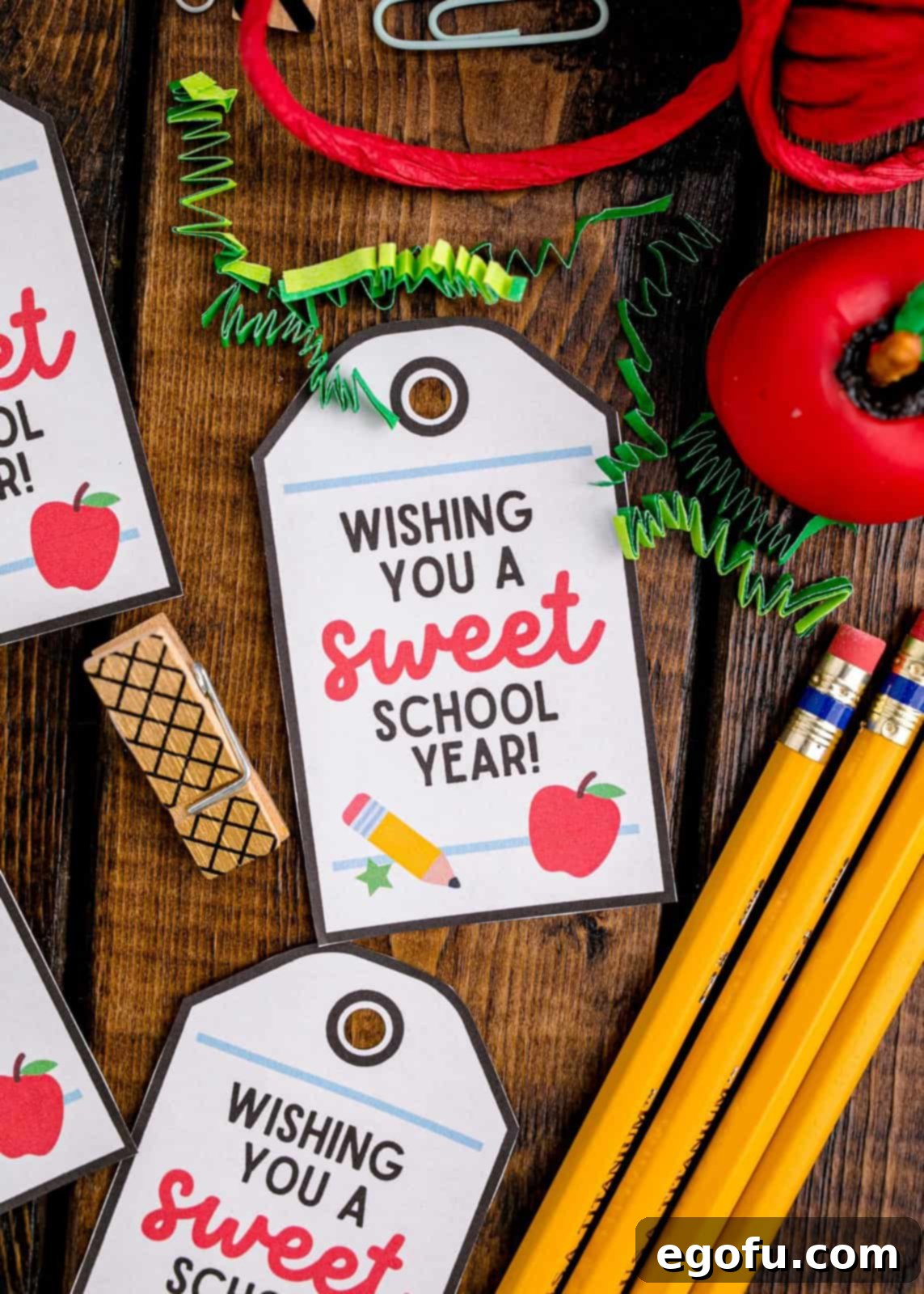 A selection of charming cut-out gift tags for bags, resting on a wooden board surrounded by various school supplies, ready for personalizing treats.