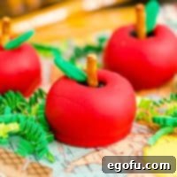Close up square image of Back-to-School Apple Shaped Oreo Truffles decorated, showcasing their vibrant red coating and green fondant leaf.