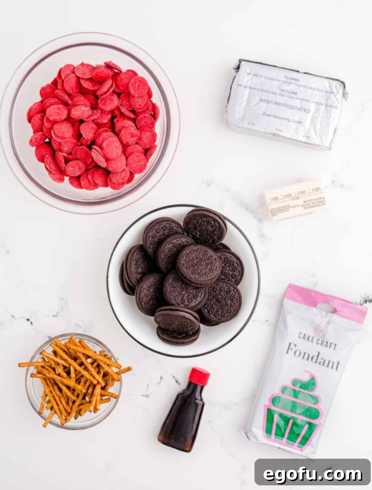 A visual display of all the ingredients needed for Back-to-School Apple Shaped Oreo Truffles: Oreo cookies, cream cheese, butter, vanilla extract, red candy melts, pre-made green fondant, and small pretzel sticks, neatly arranged for preparation.