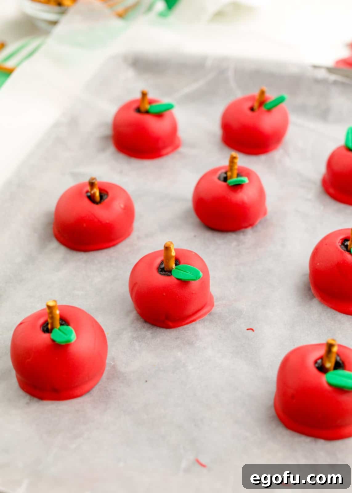 Finished Back-to-School Apple Shaped Oreo Truffles, neatly arranged on a baking sheet with white parchment paper, showcasing their perfect red coating and delicate green fondant leaves.