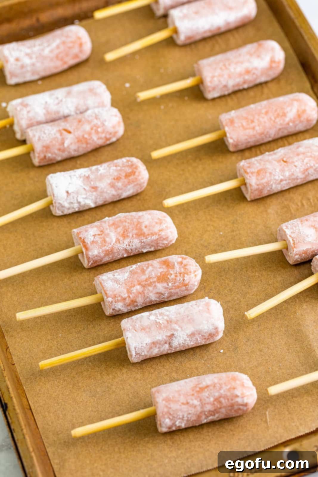 Skewers inserted into hot dogs on parchment lined sheet tray.