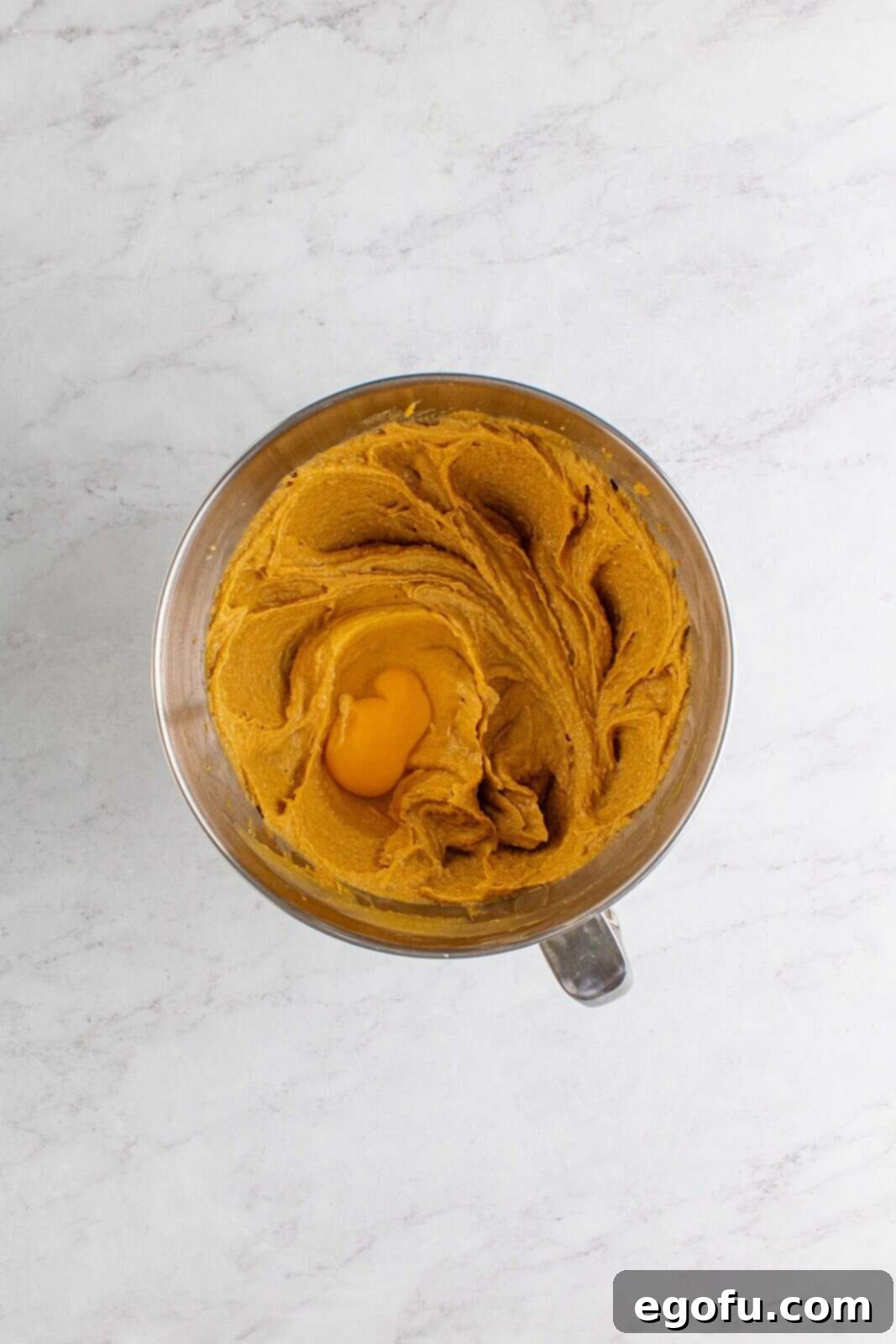 Eggs being beaten into the peanut butter mixture in the bowl of a stand mixer, one at a time.