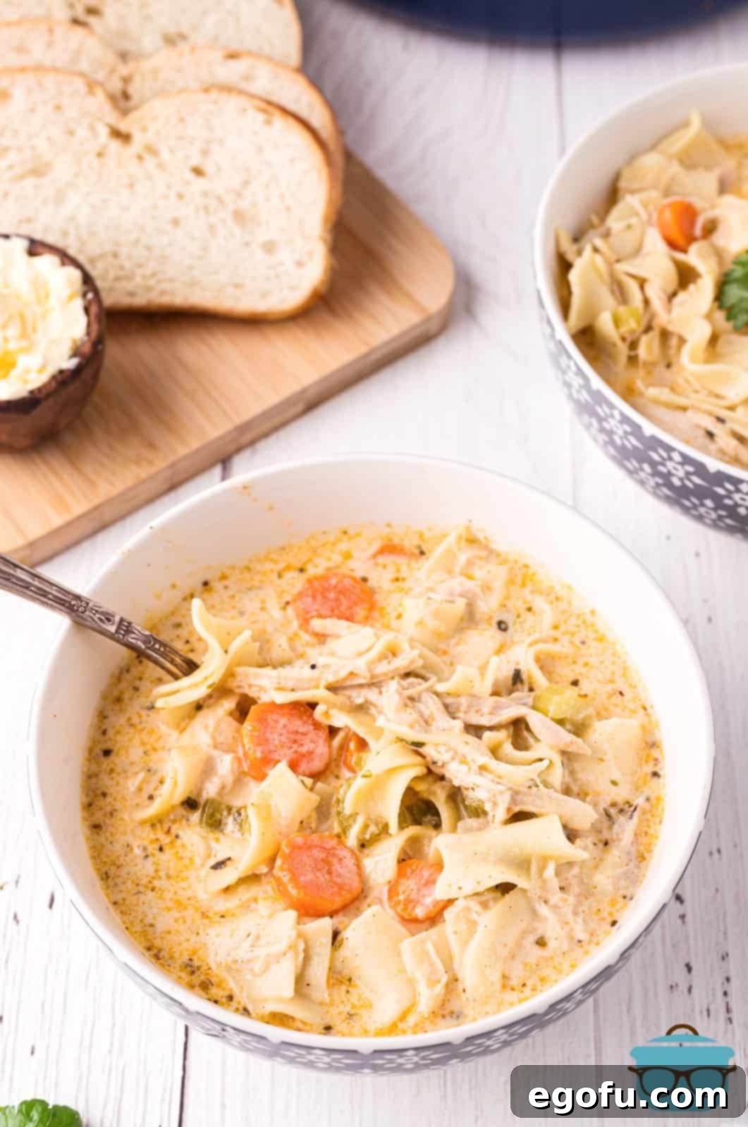 Creamy Chicken Noodle Soup in bowl with spoon and bread in background.