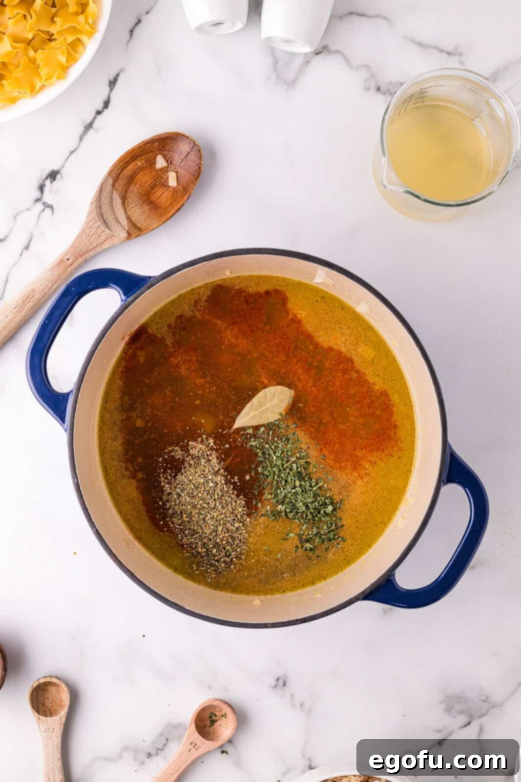 Chicken broth, bay leaf, garlic powder, parsley, salt, pepper, and smoked paprika added to dutch oven with vegetables.