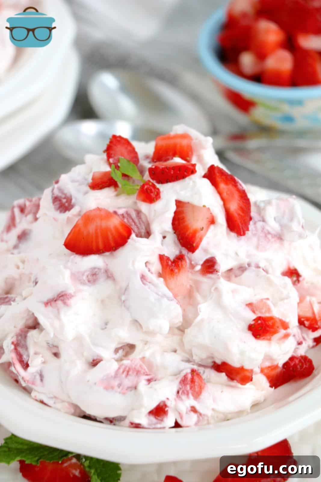 A beautiful white bowl filled with Strawberry Cheesecake Fluff, garnished with fresh whole strawberries and a sprig of mint, ready to be served.