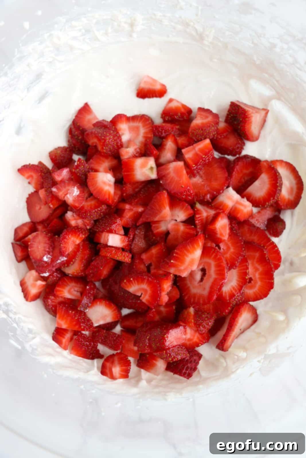 Diced fresh strawberries being gently added into the creamy cheesecake and Cool Whip mixture in a large mixing bowl.