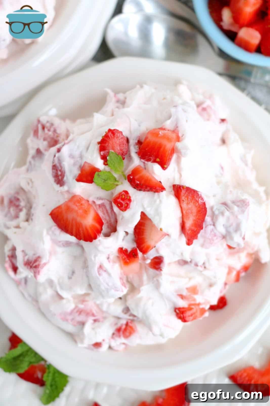 A stunning overhead shot of the finished Strawberry Cheesecake Fluff, beautifully garnished with fresh strawberries and vibrant green mint leaves, showcased in a serving bowl.