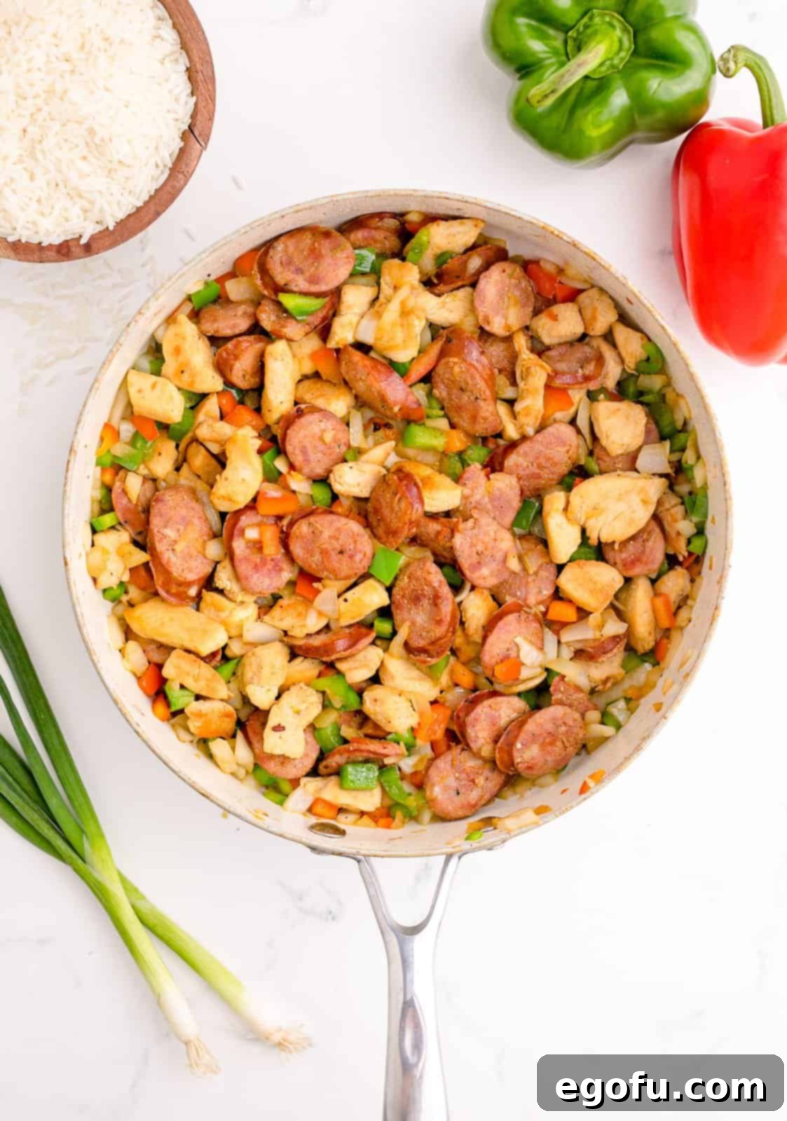 Diced onion, bell peppers, and celery added to the browned meats and stirred in the pot.