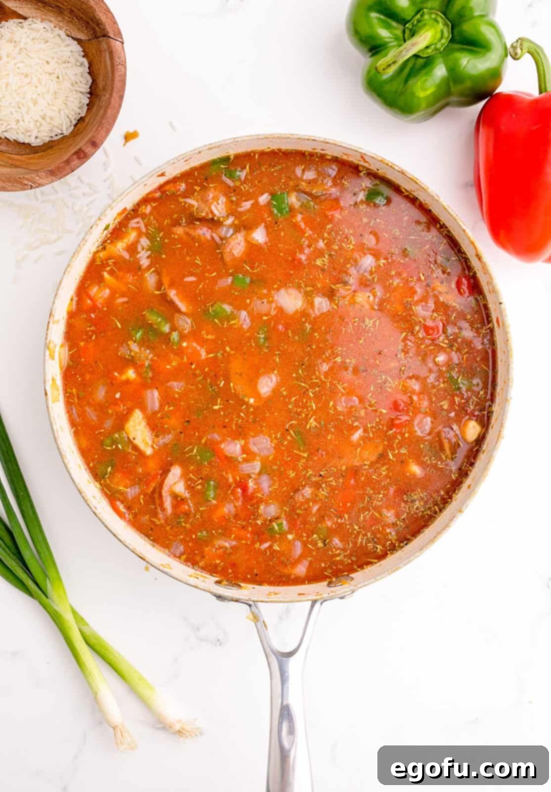 White rice and chicken broth added and stirred together in the pan, preparing for simmering.