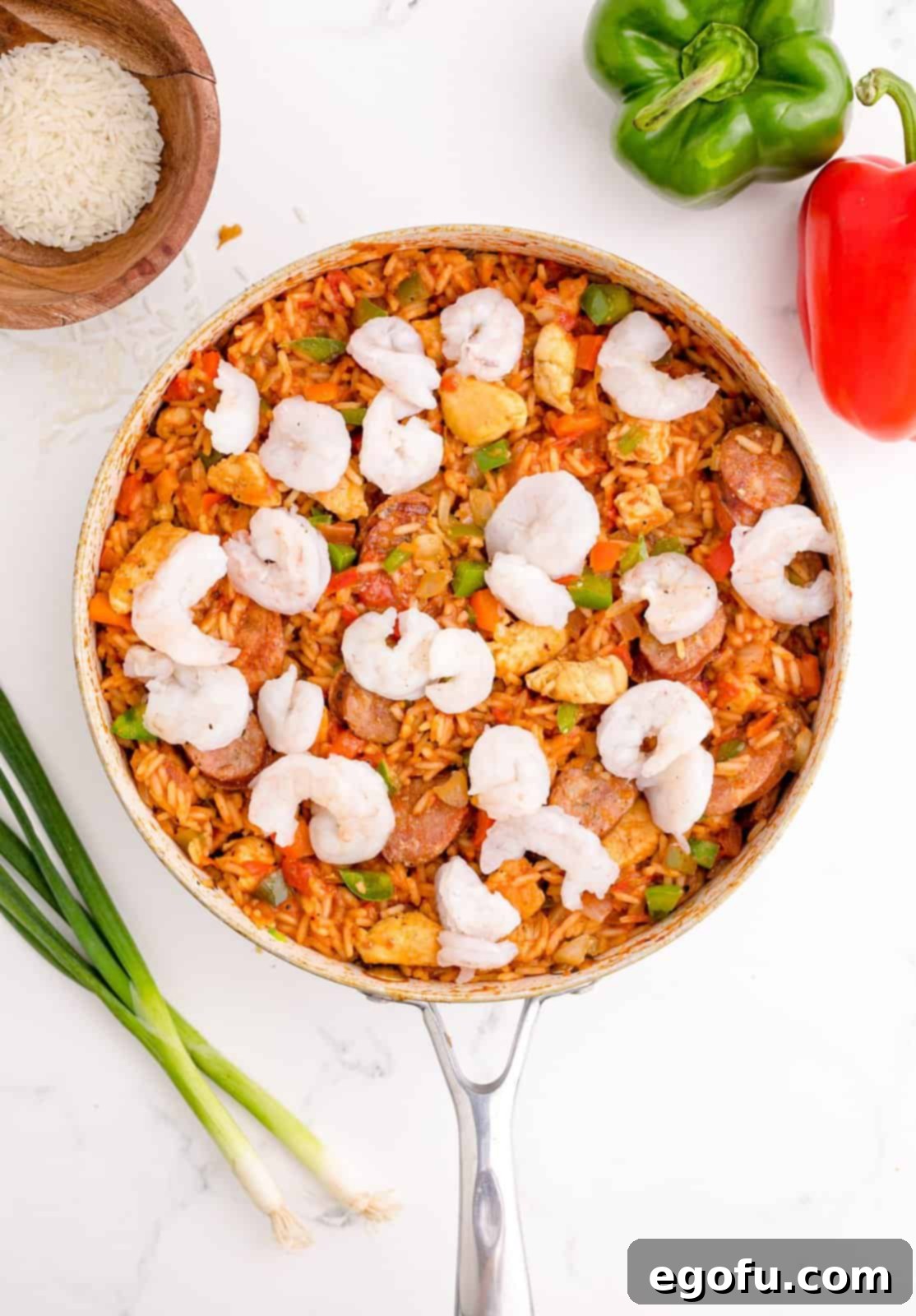 Peeled and deveined shrimp being added to the Jambalaya mixture in the pan.