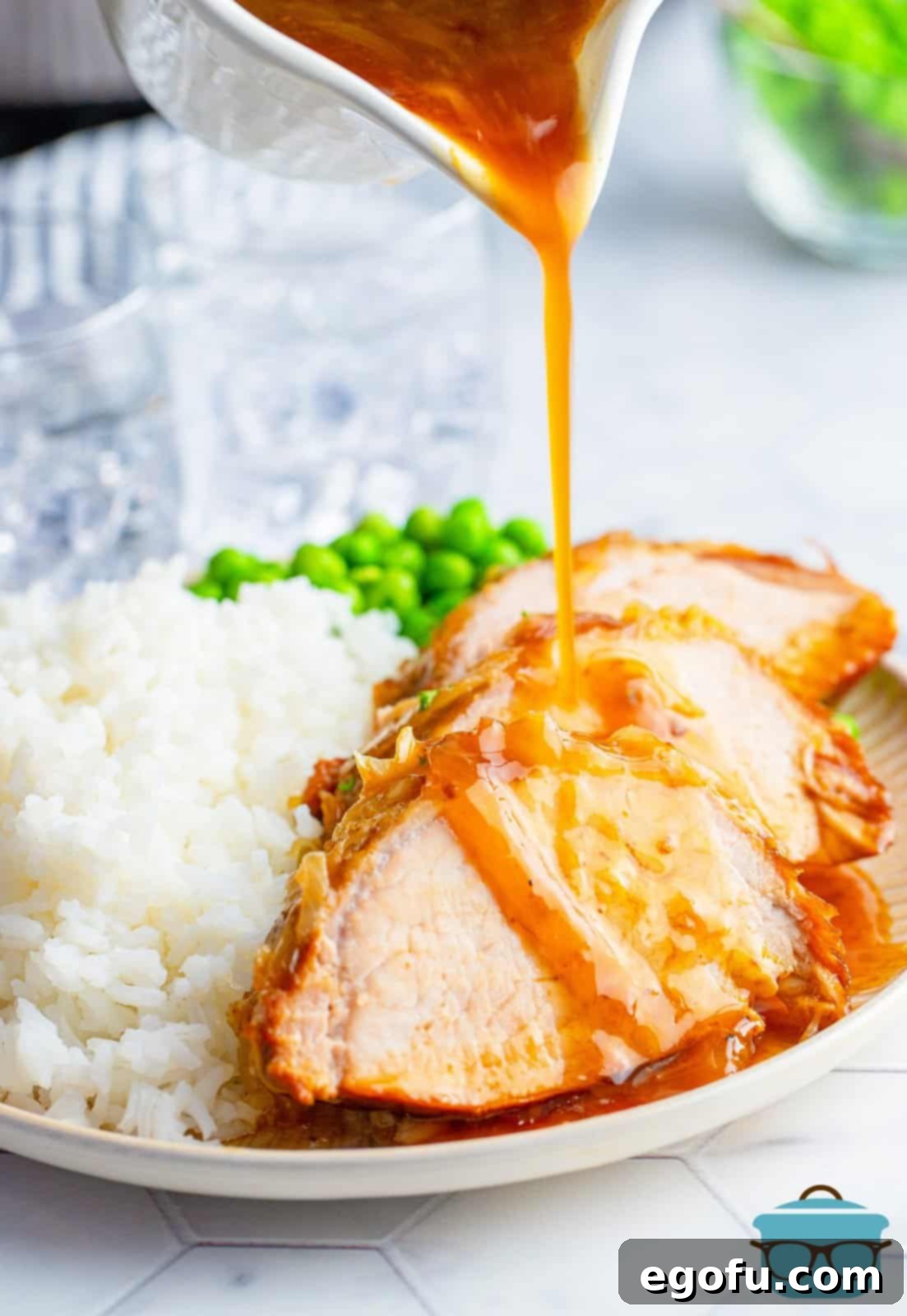 Effortless Crock Pot Pork Loin 10 Gravy being poured over sliced up Crock Pot Pork Loin on white plate with sides.