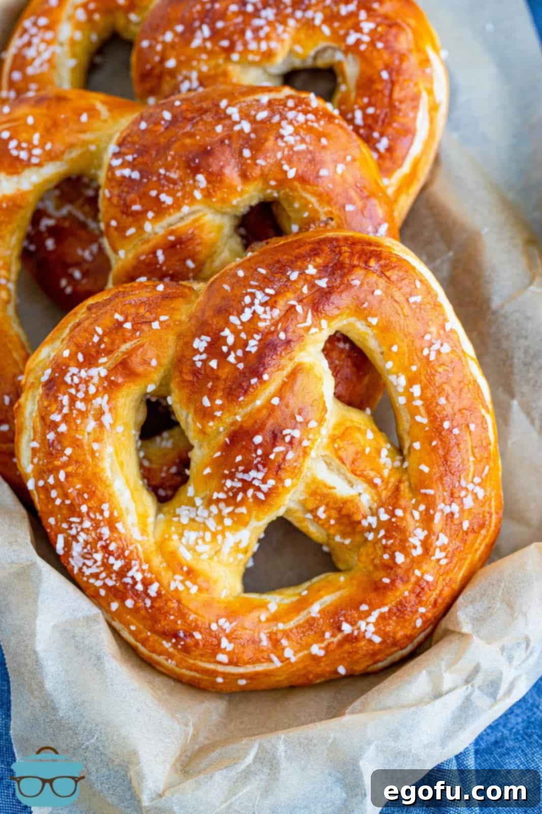 Overhead shot of freshly baked Homemade Soft Pretzels arranged on a parchment-lined tray, golden brown and glistening with butter and salt.