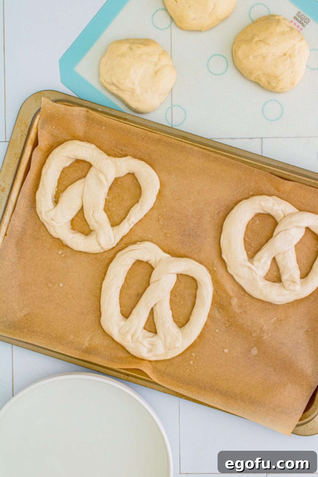 Unbaked pretzels arranged with space on a parchment-lined baking sheet, ready for the oven.