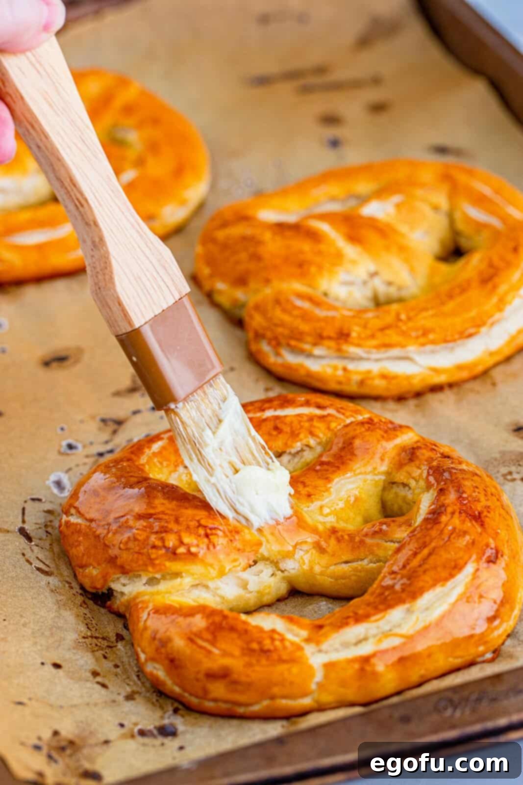 Freshly baked pretzels being brushed with melted butter for a glossy finish.