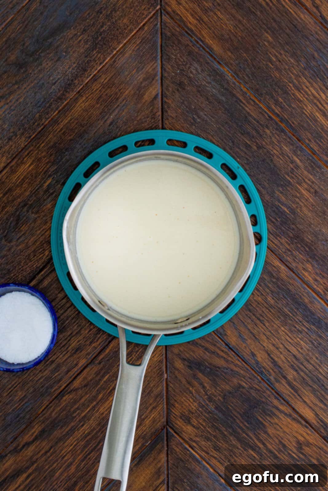 Milk slowly being whisked into the butter and flour mixture in a saucepan, gradually thickening into a sauce base.