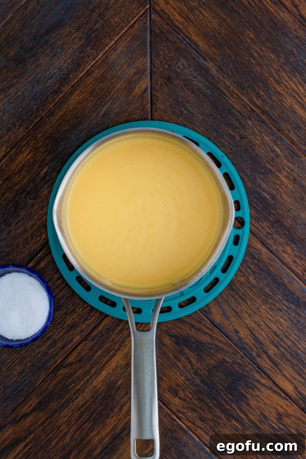 Shredded cheddar cheese being stirred into the hot sauce in a saucepan until fully melted and smooth.