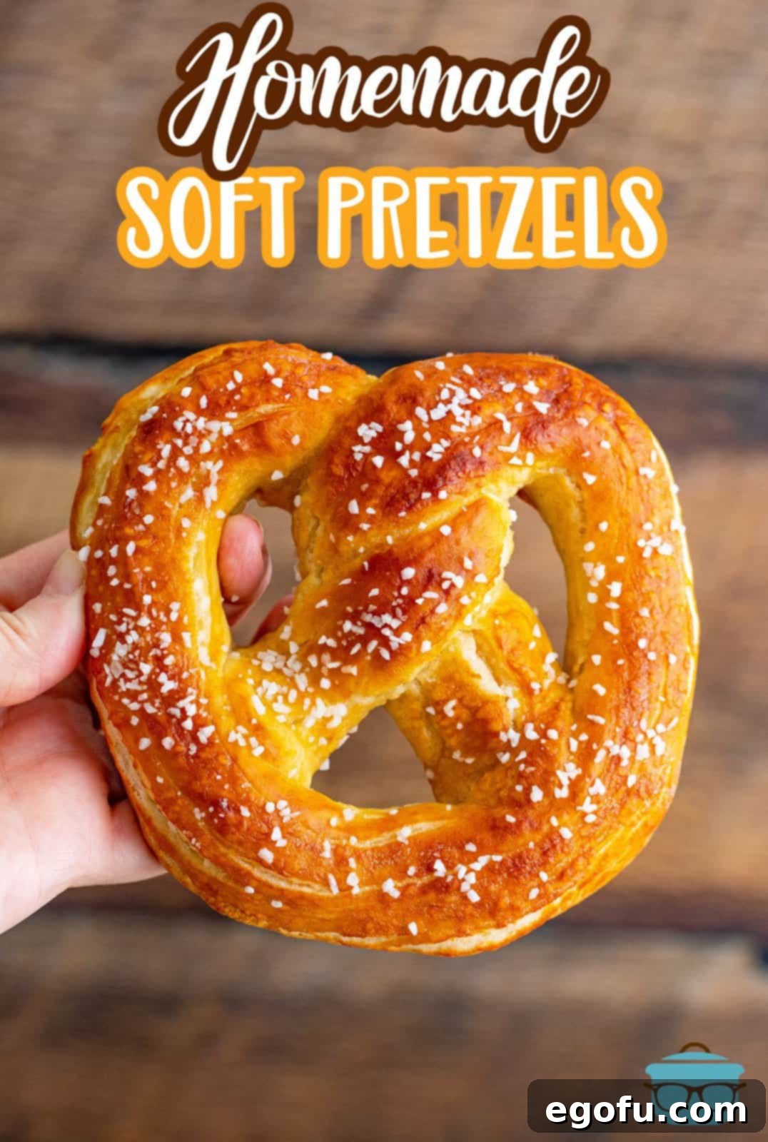 Close-up of a hand holding a golden, perfectly shaped Homemade Soft Pretzel, ready to be dipped.
